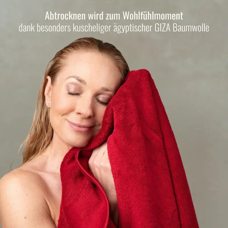 Frau hält ein rotes Bomlins Handtuch aus ägyptischer GIZA Baumwolle sanft an ihr Gesicht und genießt das weiche, kuschelige Material