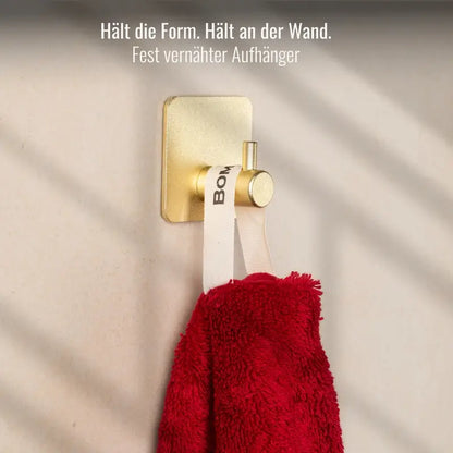 Rotes Bomlins Handtuch mit fest vernähtem Aufhänger an einem goldenen Wandhaken befestigt