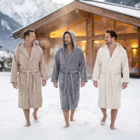 Herren in drei verschiedenen Bomlins Bademänteln aus GIZA Baumwolle (Cashmere Beige Grau Naturweiß) gehen barfuß durch den Schnee vor einer Berghütte.
