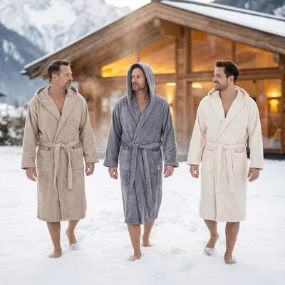 Herren in drei verschiedenen Bomlins Bademänteln aus GIZA Baumwolle (Cashmere Beige Grau Naturweiß) gehen barfuß durch den Schnee vor einer Berghütte.